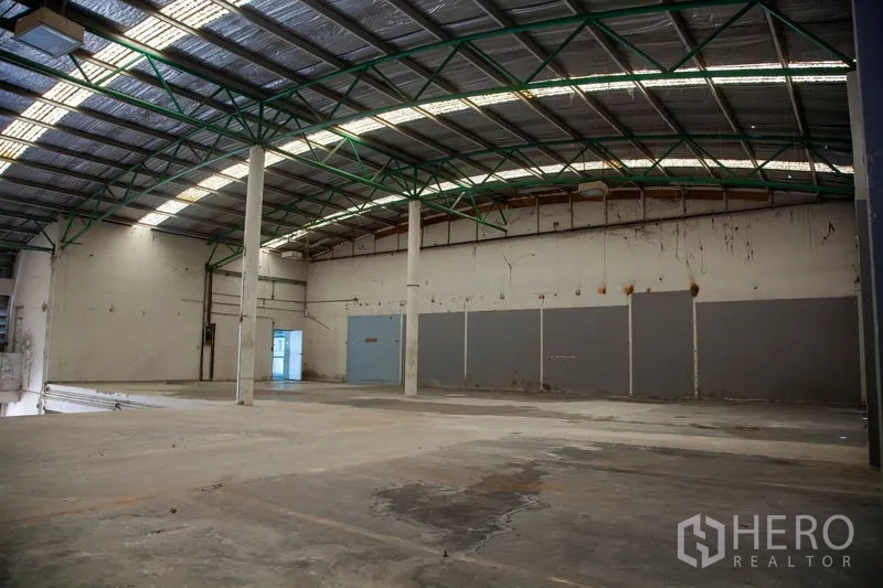 Warehouse for rent in Prawet, Bangkok - Wide production floor with curved roof, green trusses and ample lighting in a Bangkok warehouse.