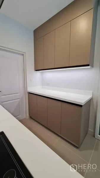 Detached House for rent in Samut Prakan - Kitchen storage cabinets with long white countertop and under-cabinet lighting.