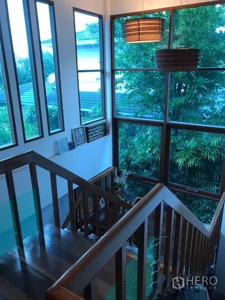 Detached House for sale in Lat Phrao, Bangkok - Staircase landing with large corner windows overlooking mature greenery and neighboring roofs.