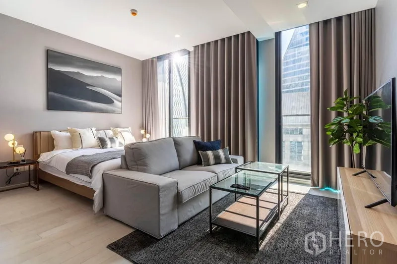 Condominium for rent in Pathum Wan, Bangkok - Overall layout showing bed, sofa, TV unit and expansive glazing with curtains.