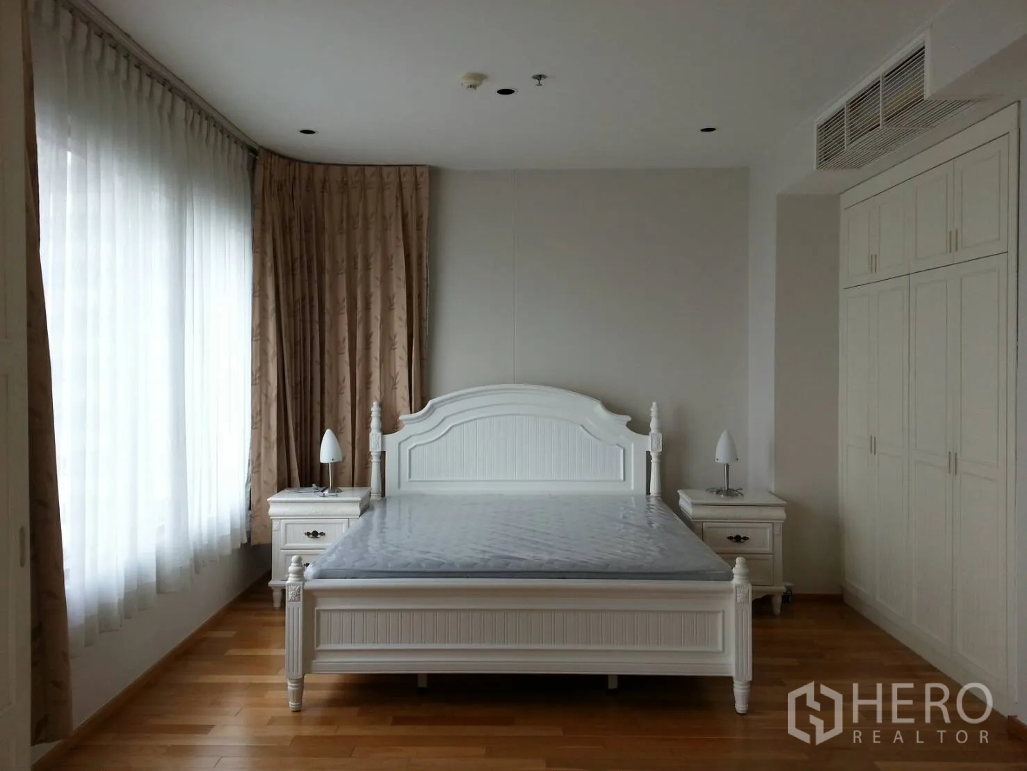 Condominium for rent in Khlong Toei, Bangkok - Spacious bedroom with large bed, bedside tables, built-in wardrobes, and corner windows with sheer curtains.