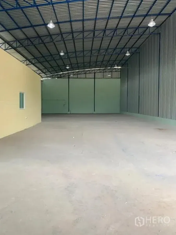 Factory for rent in Khlong Luang, Pathum Thani - Wide open factory floor under high steel trusses with high-bay lighting and a rear roller shutter.