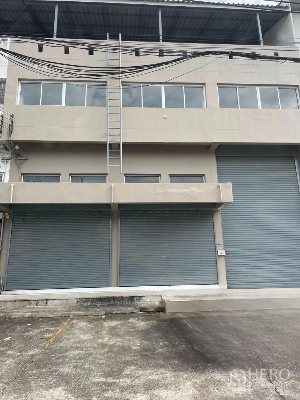 Warehouse for rent in Bang Phli, Samut Prakan - Street-facing warehouse facade in Bang Phli, Samut Prakan with multiple roller shutters, a loading apron and rooftop overhang.