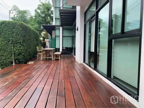 สำนักงานที่บ้าน ขายในWang Thonglang, Bangkok - ชานไม้กว้างข้างแนวรั้วพุ่ม พร้อมโต๊ะและม้านั่ง กลางประตูกระจกสูงจรดเพดาน