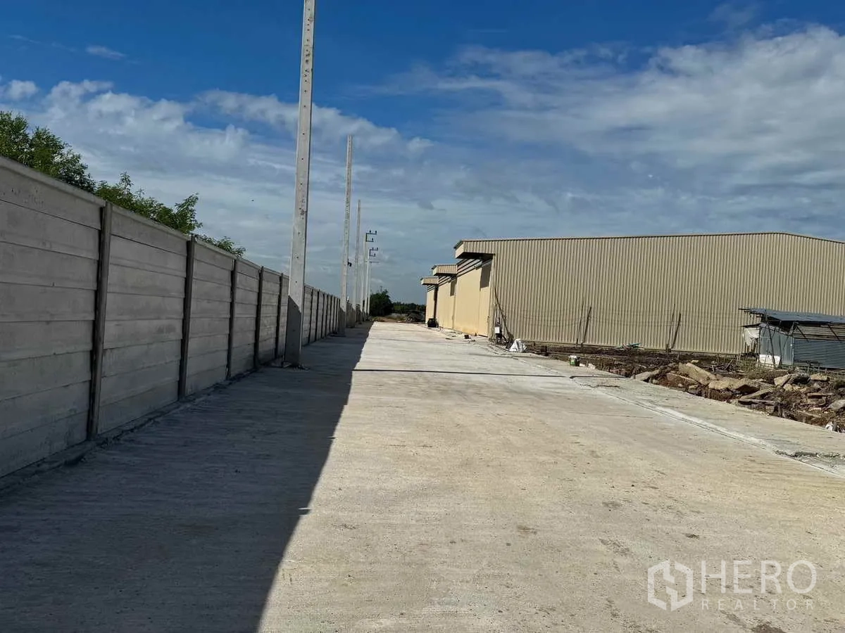 Warehouse for rent in Pak Kret, Nonthaburi - Concrete access road inside the compound with perimeter wall and warehouse buildings.