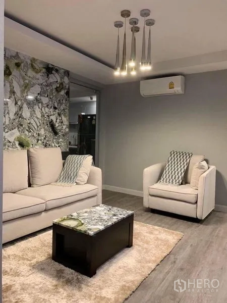 Condominium for sale in Khlong Toei, Bangkok - Cozy living space showing sofa set, single armchair, marble coffee table, area rug and wall-mounted A/C.