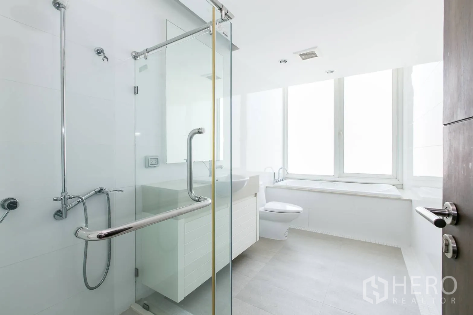 Condominium for rent or sale in Khlong Toei, Bangkok - Spacious white bathroom with glass shower, window-side bathtub and vanity.