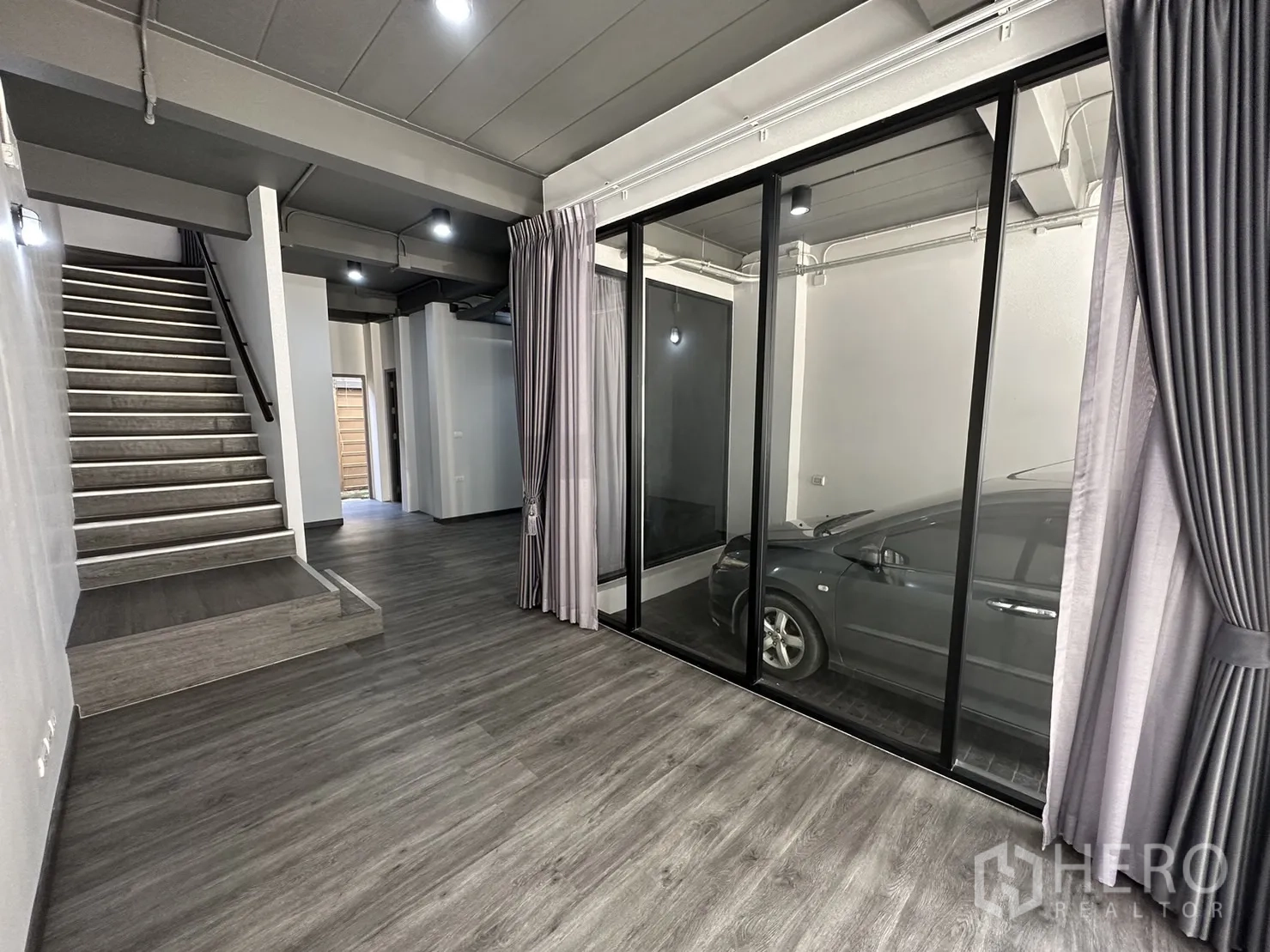 Home Office for rent or sale in Suan Luang, Bangkok - Ground floor room with floor-to-ceiling glass looking into a covered parking bay and an open staircase.