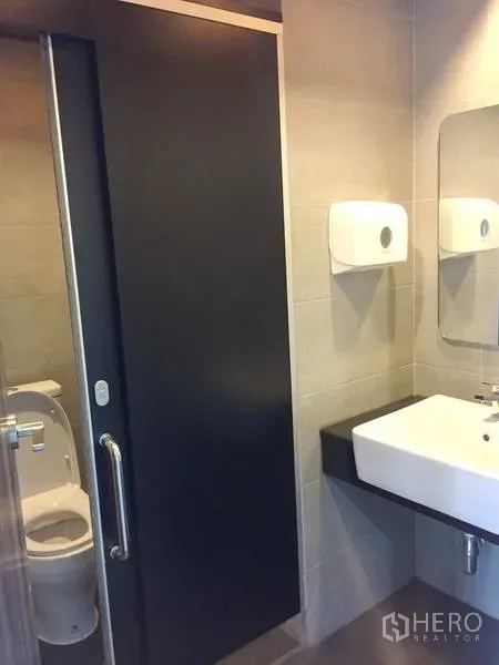 Office Space for rent in Khlong Toei, Bangkok - Modern office restroom with tiled walls, sliding door, countertop sink and toilet.