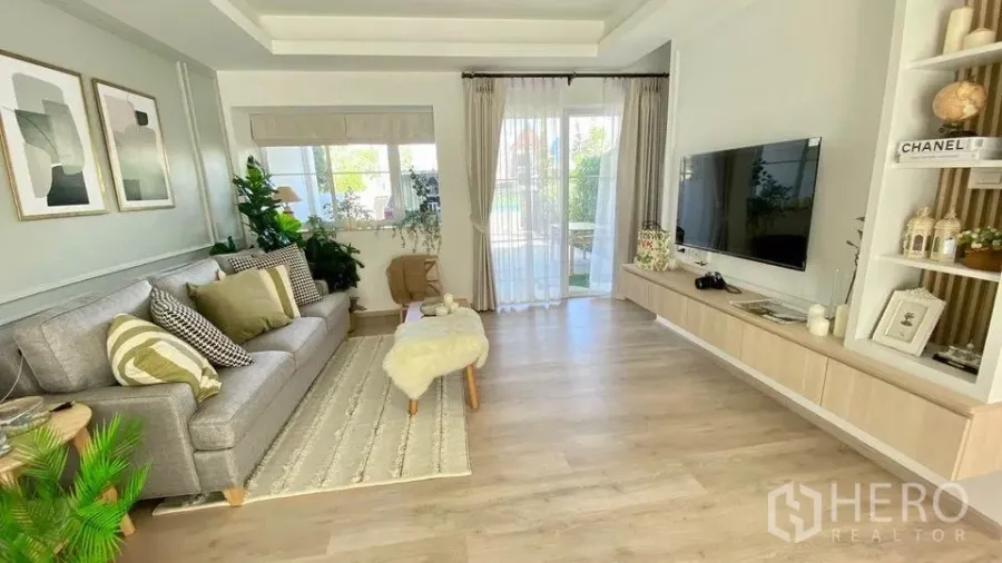Townhouse for rent in Prawet, Bangkok - Living room with wall-mounted TV, sliding glass doors to the terrace and light wood flooring.