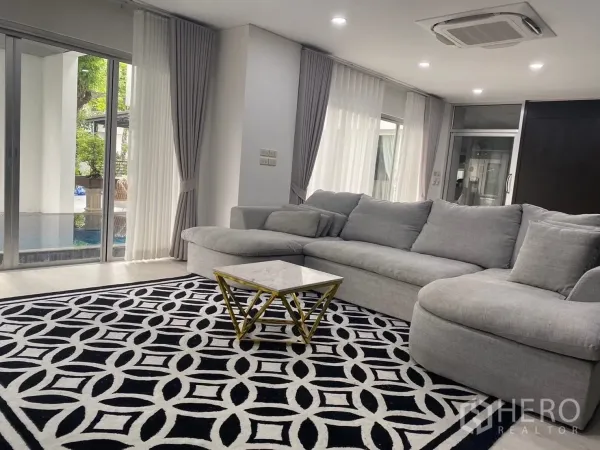 Detached House for rent in Suan Luang, Bangkok - Spacious living area with an L-shaped grey sofa and pool view through glass doors.
