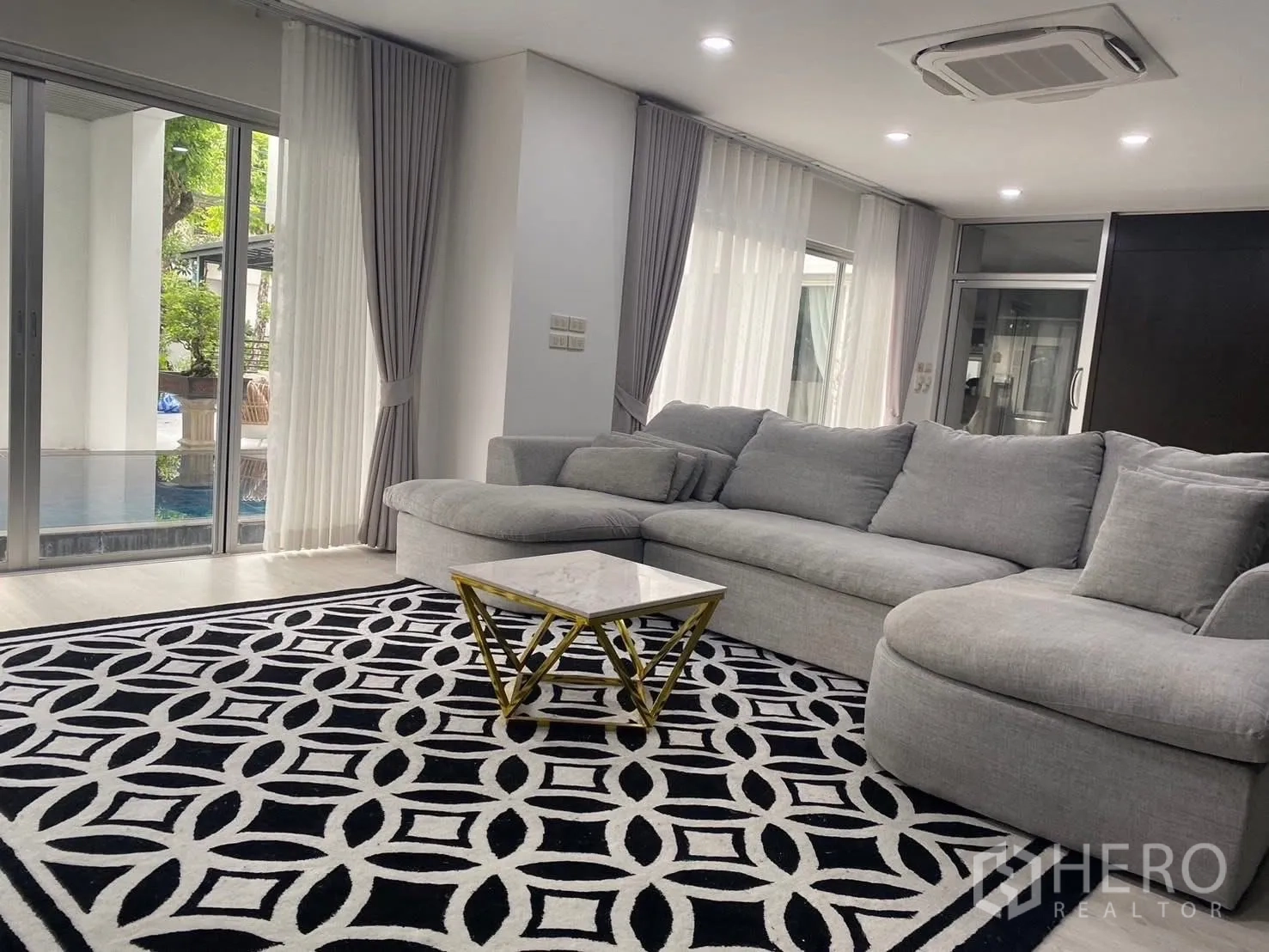 Detached House for rent in Suan Luang, Bangkok - Spacious living area with an L-shaped grey sofa and pool view through glass doors.