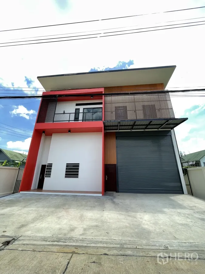 Factory for rent or sale in Lam Luk Ka, Pathum Thani - Two-storey mini factory facade with red frame, balcony, and a large gray roller shutter.