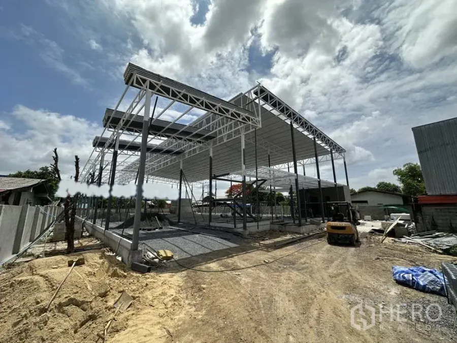 Warehouse for rent in Lat Krabang, Bangkok - Steel-frame warehouse under construction with high gable roof and open span on a gravel yard in Lat Krabang, Bangkok.