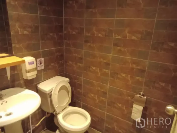 Detached House for rent in Phaya Thai, Bangkok - Bathroom with brown tiled walls, sink and toilet.