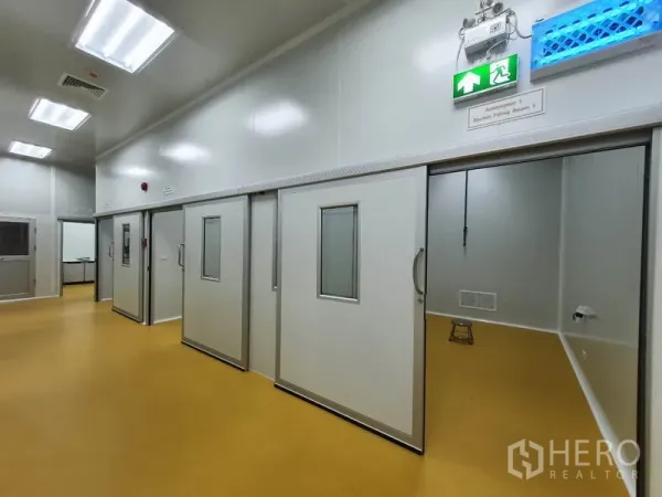 Factory for sale in Lam Luk Ka, Pathum Thani - Corridor of cleanroom suites with sliding doors and an illuminated emergency exit sign.