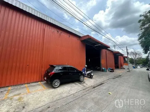 Warehouse for rent in Bang Kapi, Bangkok - Red metal-clad warehouse exterior with wide loading bay, open door and parking on a concrete street.
