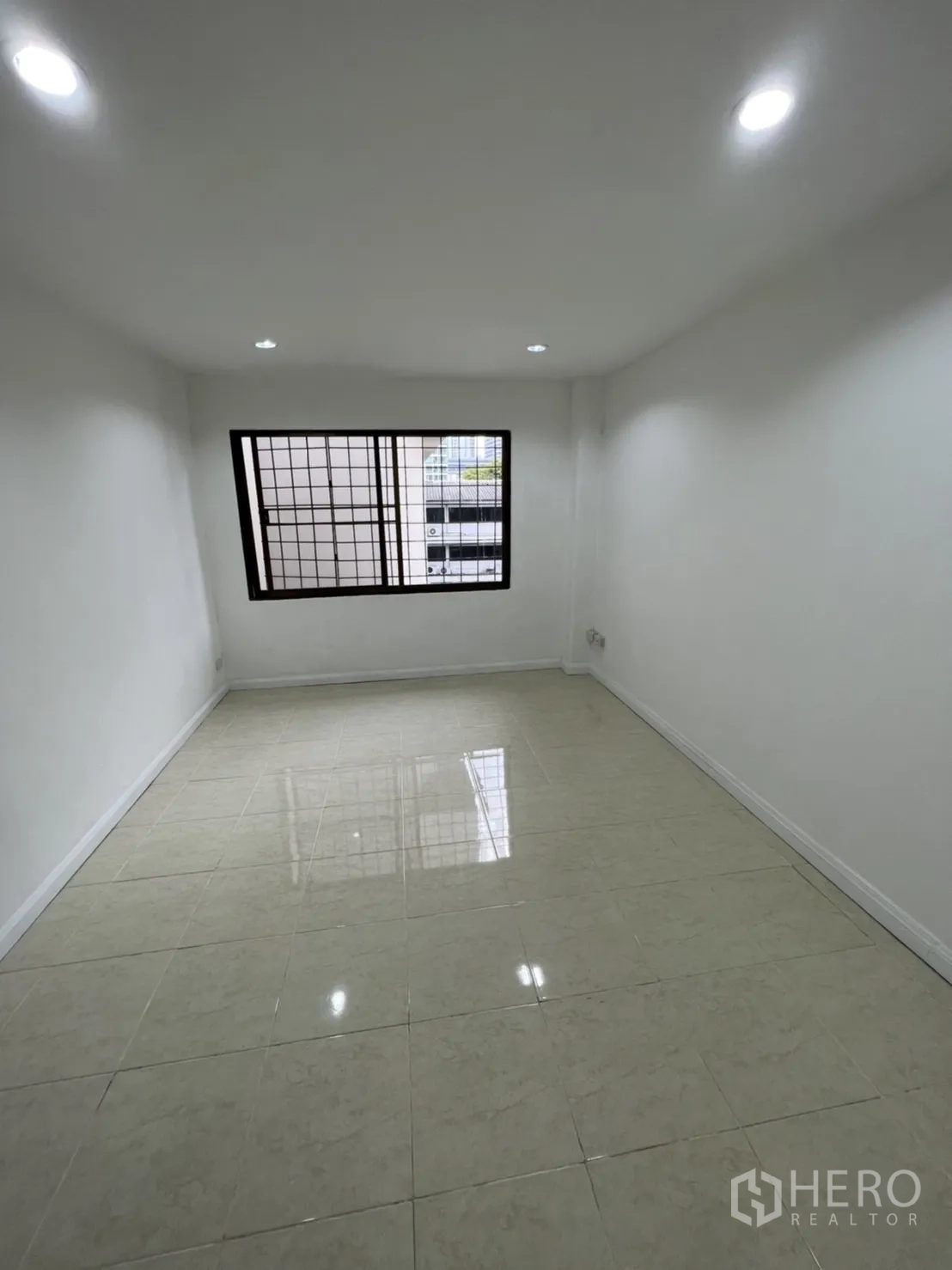Shophouse for rent in Watthana, Bangkok - Compact office-style room with window bars, recessed lights and shiny tiles.