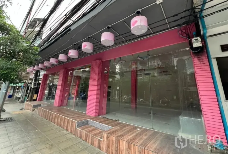 Shophouse for rent in Watthana, Bangkok - Wide glass frontage with pink columns and a raised wooden platform along the sidewalk.