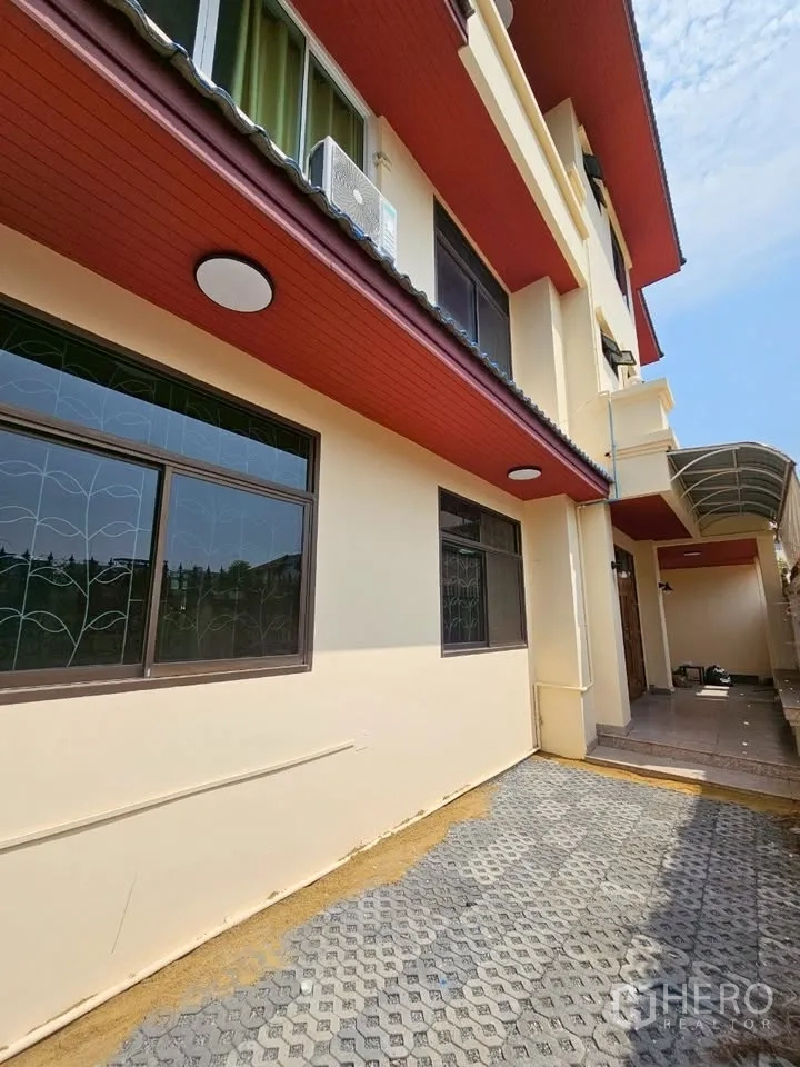 Home Office for rent in Wang Thonglang, Bangkok - Exterior side of cream building with red eaves, barred windows and a paved yard.