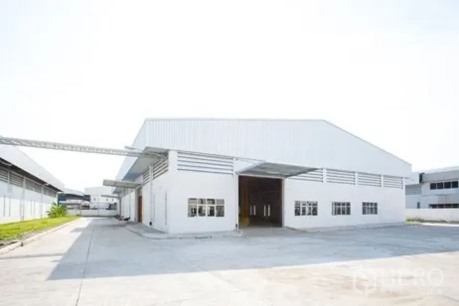 Factory for rent in Bang Pakong, Chachoengsao - Front view of modern white factory warehouse with high gable roof, large roller shutter and truck access.