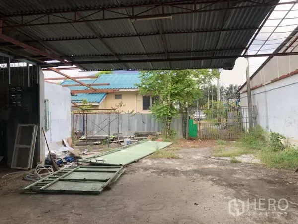 货栈 出租在Sai Mai, Bangkok - 院内带顶装卸区与宽阔空地，滑动大门部件置于地面。