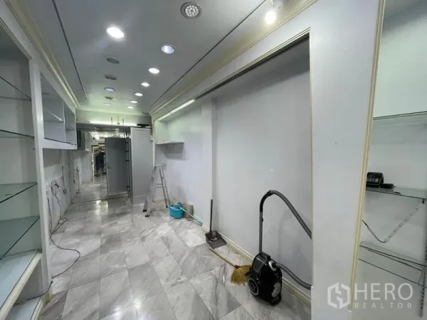 Shophouse for rent in Bang Rak, Bangkok - Narrow shop corridor showing marble tiles, display walls and cleaning equipment.