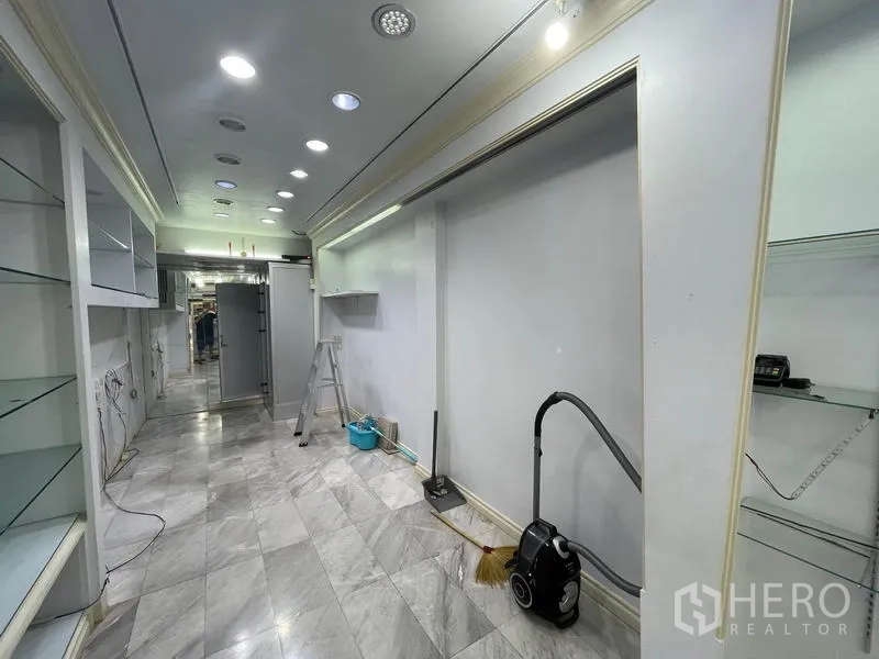 Shophouse for rent in Bang Rak, Bangkok - Narrow shop corridor showing marble tiles, display walls and cleaning equipment.