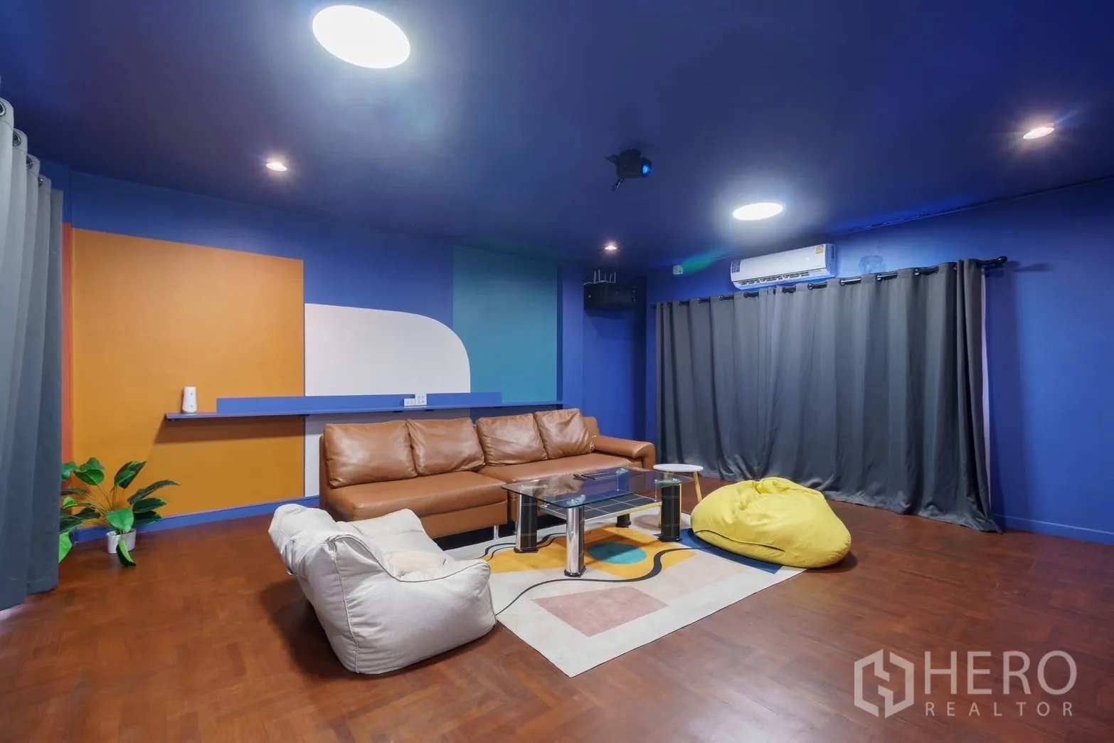 联排别墅 for rent in Watthana, Bangkok - 影音起居室，皮沙发、豆袋椅、玻璃茶几与深色窗帘。