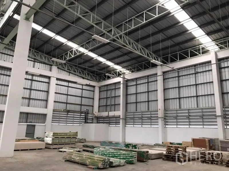 Warehouse for rent in Sai Noi, Nonthaburi - High-clear storage hall with ventilated walls and stacked building materials on the floor.