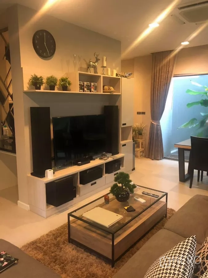 Detached House for rent in Bang Kapi, Bangkok - Cozy lounge with built-in TV wall, shelving and glass-top coffee table beside dining area.