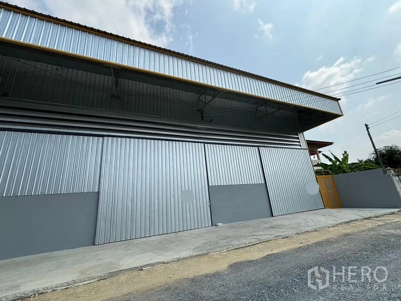 Warehouse for rent in Mueang Pathum Thani, Pathum Thani - Angled exterior view of the warehouse facade with multiple sliding doors and side gate.