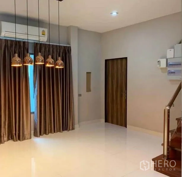 Detached House for sale in Mueang Pathum Thani, Pathum Thani - Bright living area with pendant lights, floor-to-ceiling curtains, glossy tile floor and a stairway.