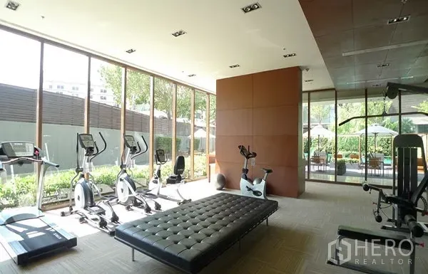Condominium for rent in Khlong Toei, Bangkok - Glass-walled fitness room with treadmills and exercise bikes overlooking a landscaped garden.