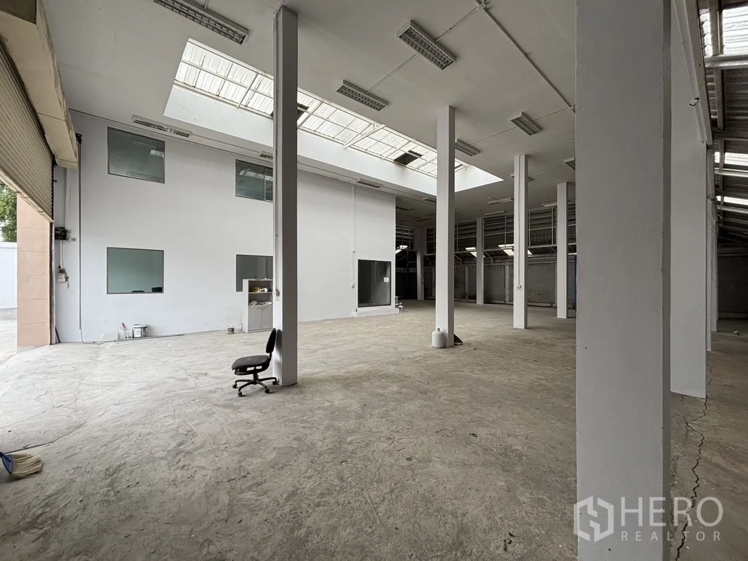 Warehouse for rent or sale in Wang Thonglang, Bangkok - Interior view toward roller shutters with rows of pillars and roof lights.