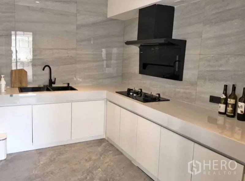 Townhouse for rent or sale in Prawet, Bangkok - L-shaped modern kitchen with white cabinetry, gas hob, and black hood.