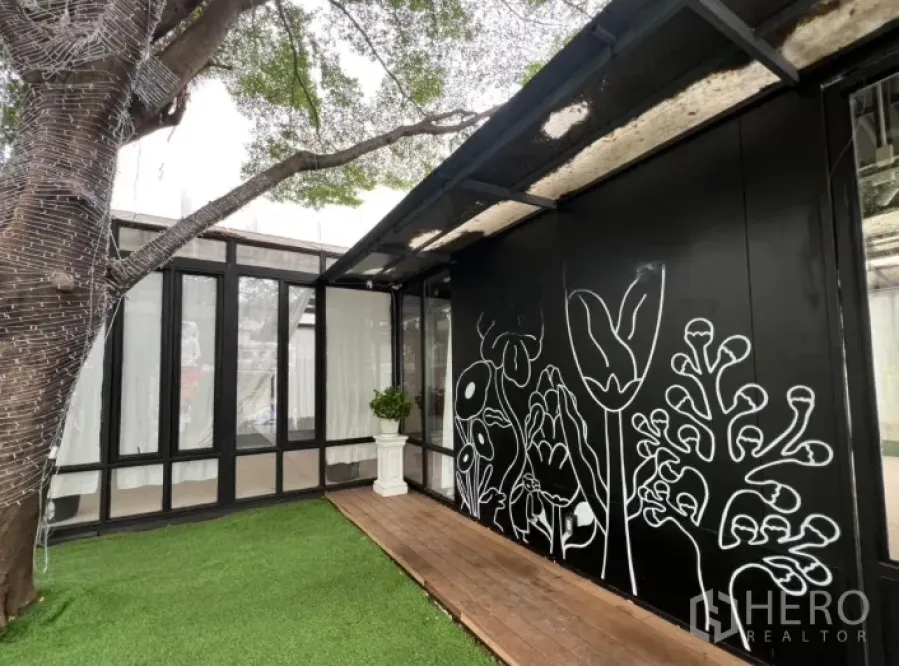 Retail Space for rent in Watthana, Bangkok - Modern black retail pavilion with floral mural, wood deck and artificial grass under a large tree.