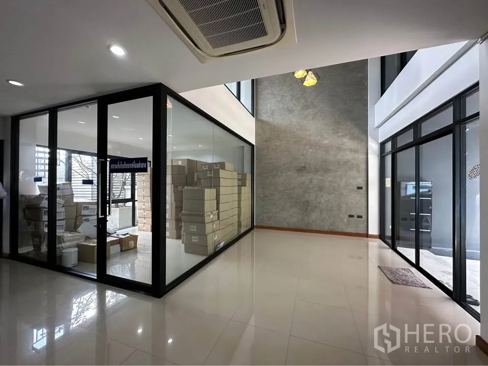 Townhouse for rent in Pak Kret, Nonthaburi - Open-plan space with polished floors, feature concrete wall, and glass cube room.