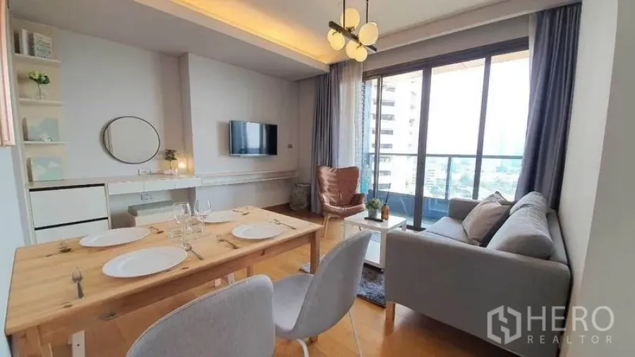 Condominium for rent in Khlong Toei, Bangkok - Open-plan living room with dining table, sofa and sliding glass doors to a balcony.
