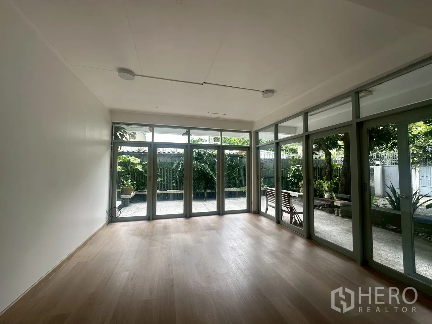 Detached House for rent in Watthana, Bangkok - Bright empty living room with light wood floors and full-height glass doors opening to the patio.