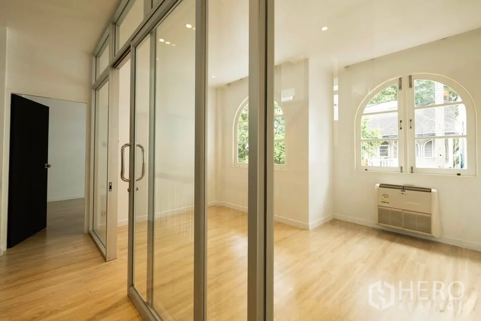 Townhouse for rent in Khlong Toei, Bangkok - Hallway featuring full-height glass sliding partitions and arched windows creating a light-filled room.