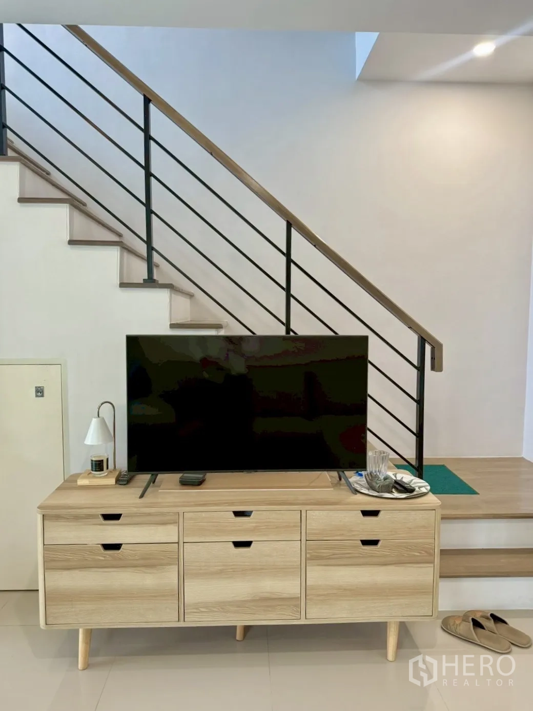 Townhouse for rent in Prawet, Bangkok - Wood TV console beneath a staircase with metal railing.