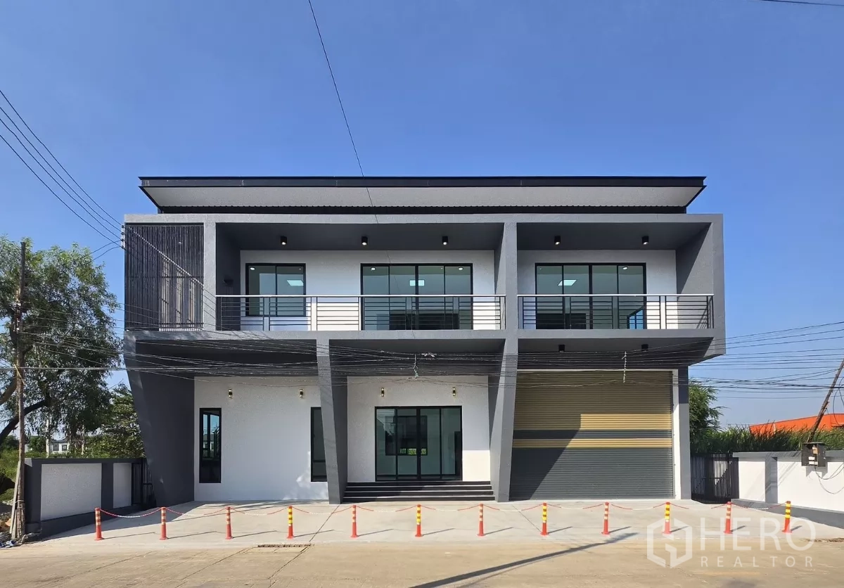 Warehouse for sale in Lam Luk Ka, Pathum Thani - Modern two-storey office-front warehouse facade in Lam Luk Ka with balcony, wide roller shutter and concrete loading yard.