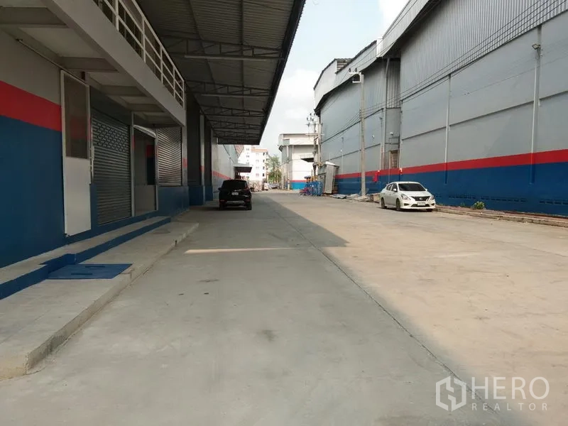 Warehouse for rent in Bang Phli, Samut Prakan - Covered loading bay and exterior driveway beside the warehouse, with shutter doors and ample turning space for trucks.
