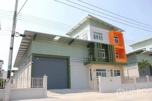 Factory for sale in Lam Luk Ka, Pathum Thani - Modern factory exterior with large roller shutter, three-storey office block and gated frontage.