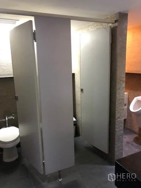 Office Space for rent in Watthana, Bangkok - Tiled restroom with toilet cubicles and adjacent urinals in an office building.
