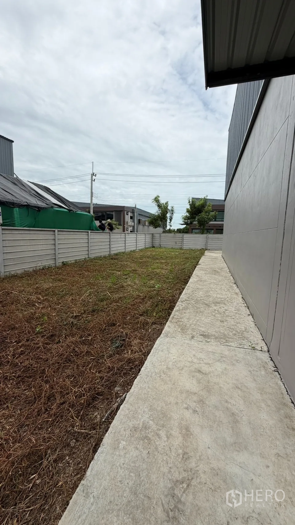 Factory for sale in Bang Len, Nakhon Pathom - Side yard with concrete walkway beside the factory wall.