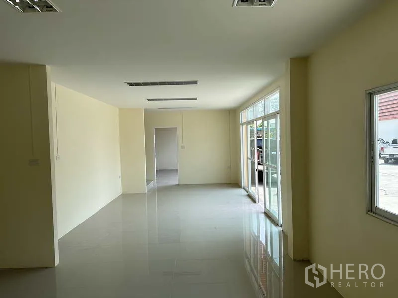 Factory for sale in Mueang Samut Prakan, Samut Prakan - Bright ground-floor office with large windows, sliding glass doors and glossy tile flooring.