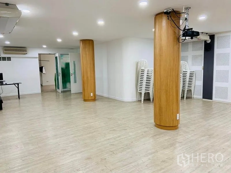 Shophouse for rent or sale in Khlong Toei, Bangkok - Large multipurpose room with wood floors, two rounded pillars, ceiling-mounted projector and stackable chairs.