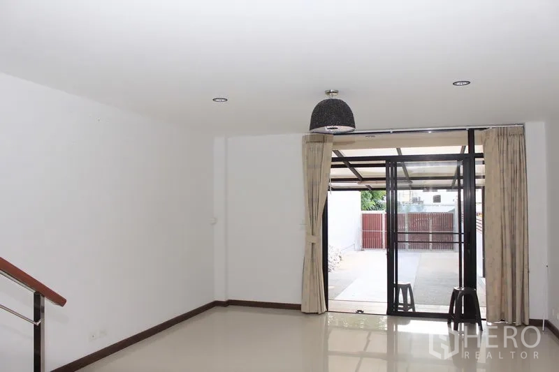 联排别墅 出租在Phaya Thai, Bangkok - 一层客厅宽敞，亮面地砖，推拉门通向带顶棚的车位与前院大门。